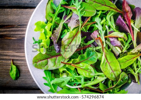 Fresh salad with mixed greens in bowl on wooden background closeup  Royalty-Free Stock Photo #574296874