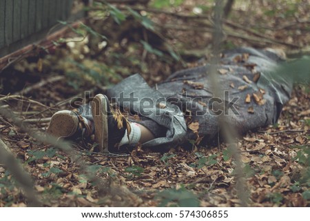 Murder victim wrapped in tarpaulin with feet protruding in leafy forest Royalty-Free Stock Photo #574306855