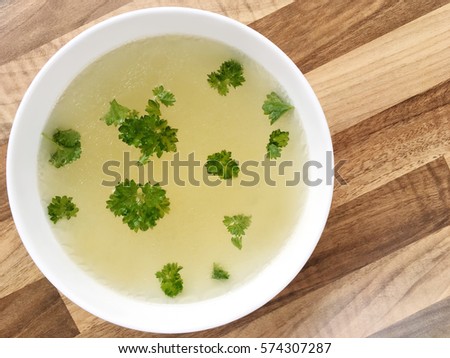 Chicken broth with green parsley in a white bowl on wooden background. Top view of chicken bouillon.