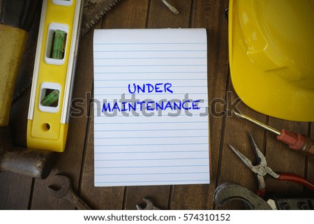 word UNDER MAINTENANCE on paper notebook with wooden background and tools.