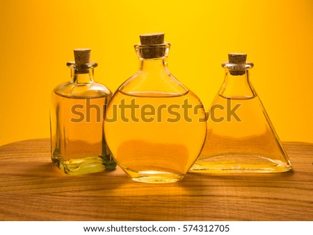 Three vintage glass bottles with yellow liquid in on wooden desk on bright orange background