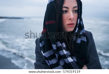 Close up portrait beautiful girl in headscarf standing on winter seacoast.Winter coat,beauty face,red lips,casual clothes,winter outfit,alone girl,girl looking away,travel girl