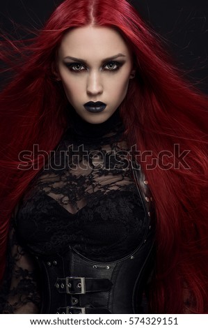 Young woman with red hair in black gothic costume on dark background