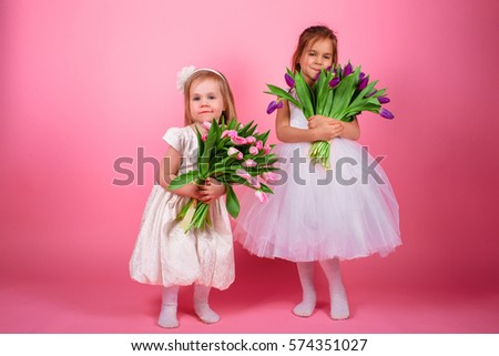 Cute emotional and smiling children with bouquet of flowers in his hands and a pink background