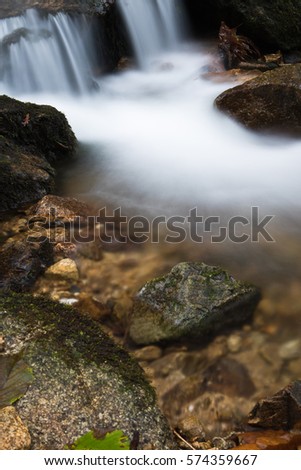 zen portrait close up of satin soft smooth river brook with rocks flowing in forest in autumn scenery 