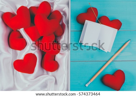 Set of red heart made from velvet fabric lay in white box with notebook and white satin on vintage blue table wood. Love and valentine's day concept.