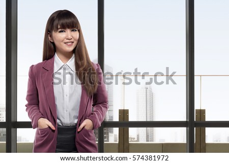 Smiling asian business woman standing in front of windows in an office