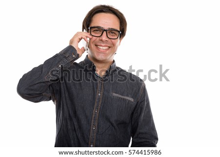 Studio shot of young happy Persian man smiling while talking on mobile phone