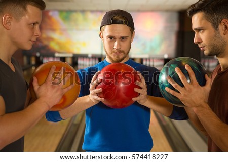 Main game. Three handsome young guys posing fiercely holding bowling balls facing each other face to face confidence winner success competitor activity entertainment players bowling club friends 
