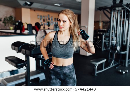 Close up portrait of fitness athletic young woman in sports clothing showing her well trained body. She puts on gloves and straightens hair before training