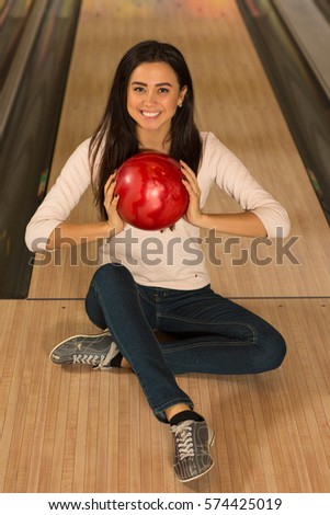Ready to bowl? Vertical top view shot of a gorgeous young female bowling player smiling to the camera holding a bowling ball sitting on the floor near bowling alley entertainment youth teen concept