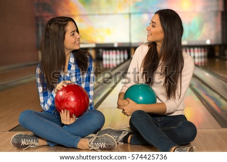 Day out with the best friend. Beautiful young women talking sitting relaxed on the floor at the bowling club near wooden alleys holding bowling balls communication gossip friends relationship concept