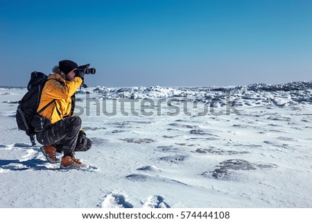 Traveler Man with backpack mountaineering. 
He is looking into the distance through binoculars. Travel Lifestyle concept mountains on background. Winter expedition vacations outdoor Royalty-Free Stock Photo #574444108