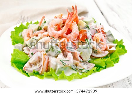 Salad with shrimp, avocado, tomatoes and mayonnaise on the lettuce in the plate, napkin, fork on background wooden plank Royalty-Free Stock Photo #574471909