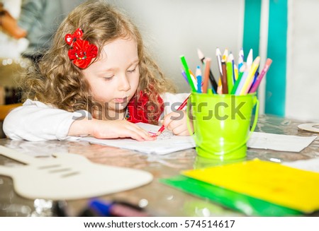 Adorable child girl drawing with colorful pencils in nursery room. Kid in kindergarten in Montessori preschool class.