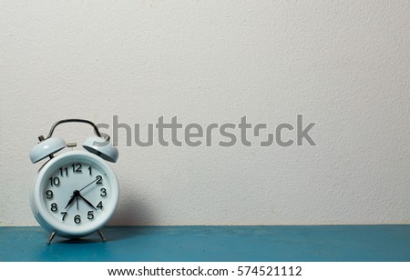 Workplace with table clock on blue table. White wall.