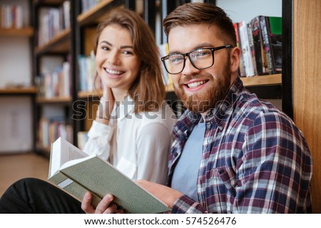 Happy young couple smiling and reading book in library