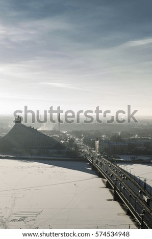A view of a city from above in winter with a new library and river between city, which is frozen and  people walking  on ice to cross the center.