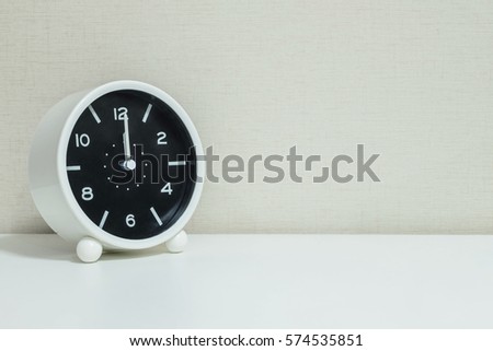 Closeup black and white alarm clock for decorate in 12 o'clock on white wood desk and cream wallpaper textured background with copy space