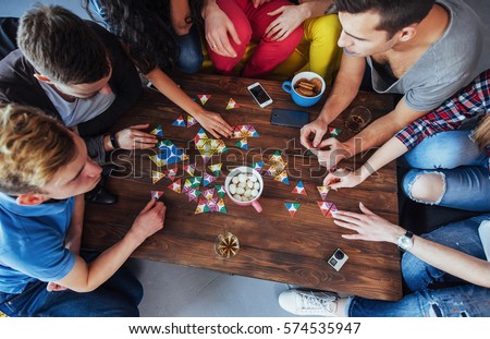 Top view creative photo of friends sitting at wooden table. Friends having fun while playing board game. Royalty-Free Stock Photo #574535947