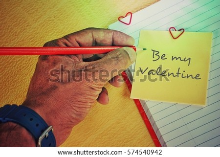 Male hand is writing on note paper and a paper clip in the shape of a heart: the concept of Valentine's Day - February 14