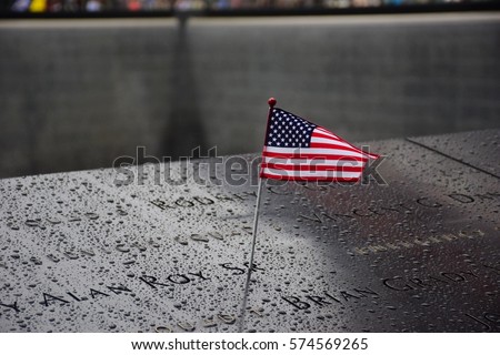 Memorial at Ground Zero Manhattan for September 11 Terrorist Attack with an American Flag Standing near the Names of Victims Engraved Royalty-Free Stock Photo #574569265