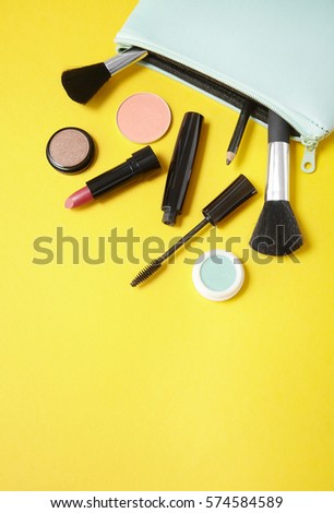 Make up products spilling out of a pastel blue cosmetics bag on to a bright yellow background with blank space below