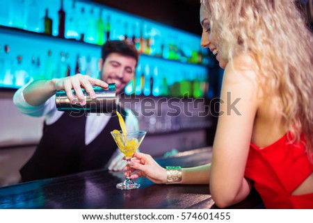 Bartender serving cocktail to young woman at counter in nightclub