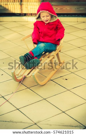 Childhood, kids imagination concept. Dissatisfied little young boy playing outside on sled but there is no snow around.