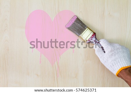 Man's hand wearing white glove holding old grunge paintbrush and painting pink heart on wooden wall, giving love concept