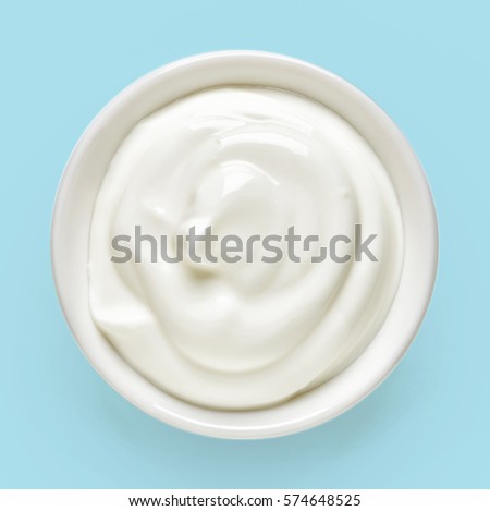 White bowl of cream on light blue background, top view
