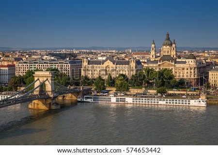 Chain Bridge over river Danube, Szechenyi Lanchid in Hungarian, on a sunny summer day. View on the Four Season Hotel, Internal affairs ministry building, and St. Stephen's Basilica in Pest. Royalty-Free Stock Photo #574653442