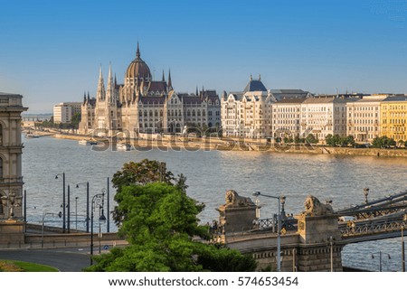 Parliament in Budapest view, with Chain Bridge with lions over river Danube, or Szechenyi Lanchid in Hungarian, on a sunny summer day.  Royalty-Free Stock Photo #574653454