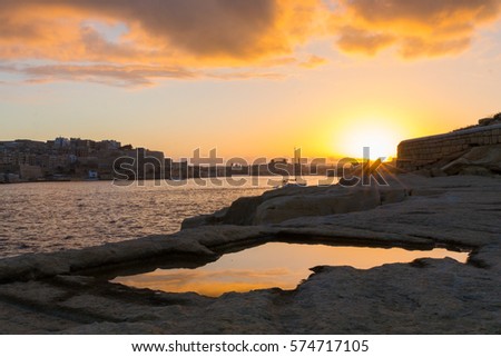 Beautiful Valletta skyline under a vibrant colorful golden sunset reflected in water across rock pools at Tigne Point, Valletta is the capital city of Malta, Europe