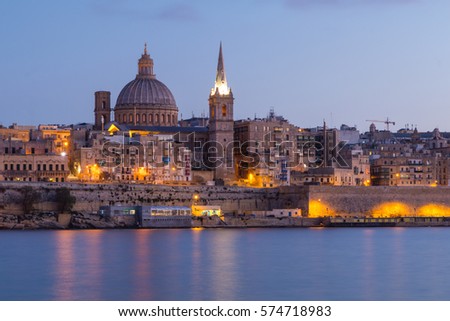 Beautiful spires and cathedral dome of the Valletta skyline under blue night sky, lights reflected in the ocean bay, Valletta, Capital city of Malta