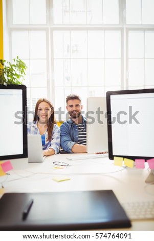Portrait of cheerful graphic designers sitting at desk in creative office