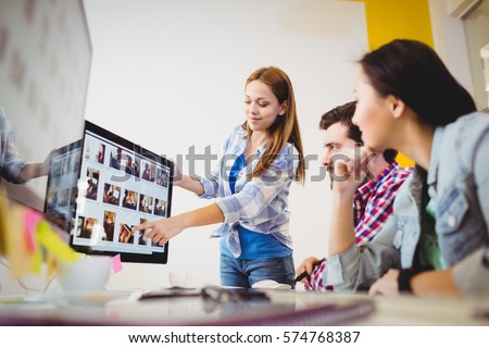 Smiling businesswoman showing computer screen to coworkers in creative office