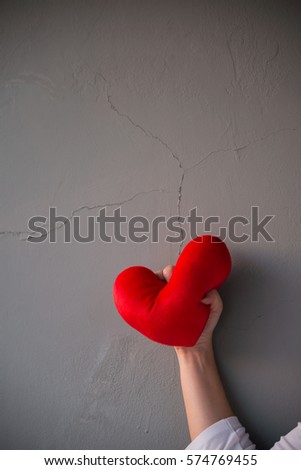 Red heart pillow was squeezed angrily over cracked grey wall background showing fail love on Valentines day occasion