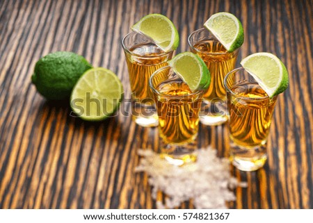 Glasses gold tequila with green lime  on a  brown wooden background ,selective focus

