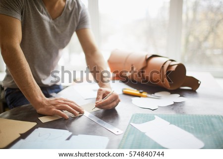 Closeup portrait of unrecognizable leather craftsman working making measupenets in patterns at table in workshop studio