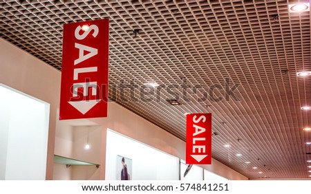 red vertical sale posters with white letters hang from grid ceiling in big shop in sale season. sale poster board at fashion clothes shopfront