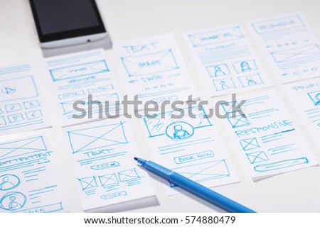 Creating mobile responsive website, wireframe sketches and blue marker pen on designer desk Royalty-Free Stock Photo #574880479