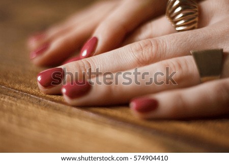 Close up of beautiful polished dark pink nails captured on the wooden table. Fingers are decorated with ring. 