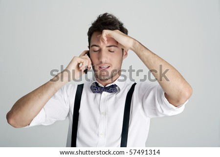Young man in bowtie and suspenders on the phone and frustrated, studio shot