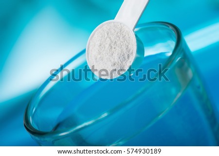 Sport supplement, creatine, hmb, bcaa, amino acid or vitamin - measure with powder over a glass of water. Sport nutrition concept. Royalty-Free Stock Photo #574930189