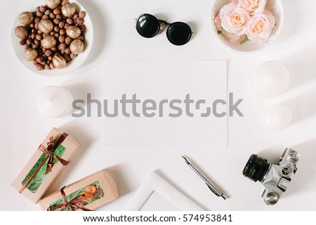 White desk with glasses, roses, candles, gifts, pen and film camera. Empty sheet in the middle. Top view, flat lay, copyspace.