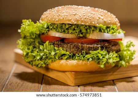 Delicious hamburger with vegetables on wooden board