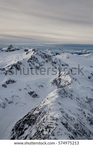 Aerial landscape view of the snow covered mountains of British Columbia, Canada. Picture taken from an airplane North of Vancouver, BC, during a cloudy winter evening.