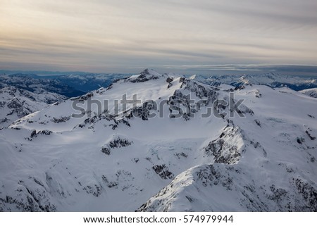 Aerial landscape view of the snow covered mountains of British Columbia, Canada. Picture taken from an airplane North of Vancouver, BC, during a cloudy winter evening before sunset.