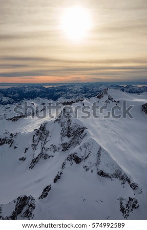 Aerial landscape view of the snow covered mountains of British Columbia, Canada. Picture taken from an airplane North of Vancouver, BC, during a cloudy winter evening before sunset.